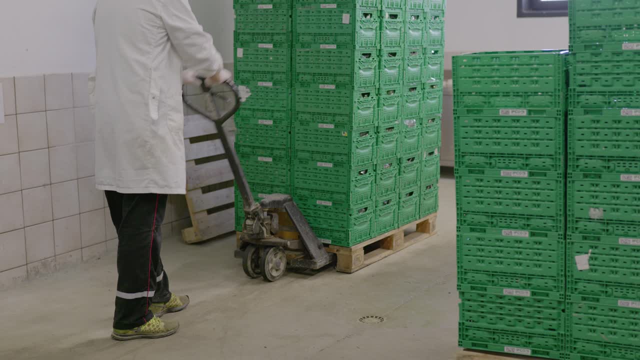 Worker using a pallet jack to move a stack of green crates in a warehouse