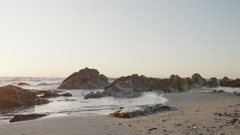 Paisaje-De-Playa-Con-Mar,-Rocas-Y-Cielo-Azul-Al-Atardecer,-En-Cámara-Lenta