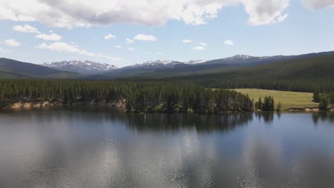 Vista-Aérea-De-La-Orilla-Del-Embalse-Del-Parque-Con-Nubes-Pico-Desierto-En-El-Fondo-En-El-Bosque-Nacional-Bighorn-En-Wyoming-En-Un-Día-De-Verano