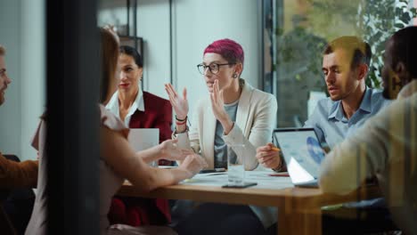 office meeting in conference room: beautiful specialist with short pink hair talks about firm strategy with diverse team of professional businesspeople. creative start-up team discusses big project