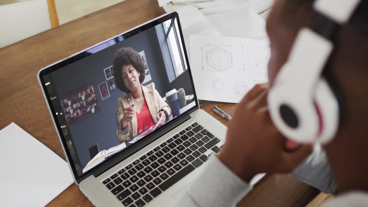 African american male college student holding notes while having a video call on laptop at home