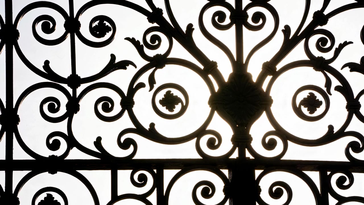 Luce solare che retroillumina un cancello in ferro battuto ornato su un balcone, proiettando volute in una silhouette netta