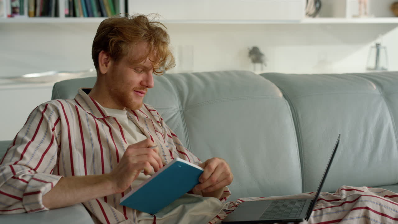 un chico sonriente aprendiendo en línea en casa el fin de semana. trabajo de estudiante de jengibre tomando notas