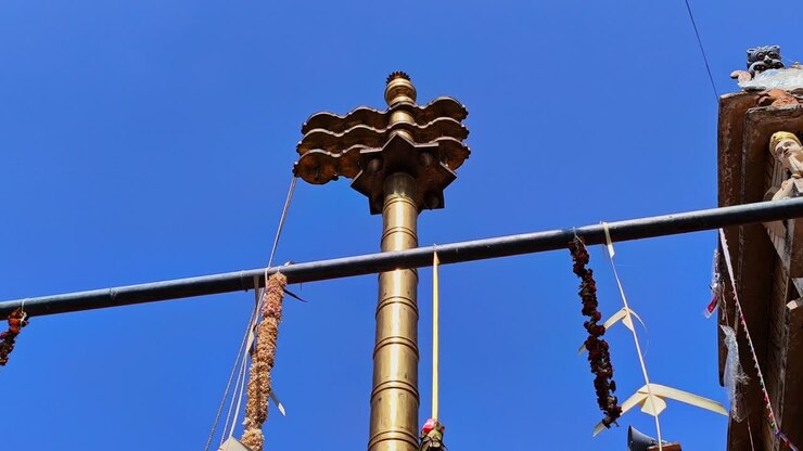 Brass Dwajasthambam (Temple flag pole) with Temple gopuram and background blue sky at kodangal, india. day time, low angle shot, stable shot, 4k