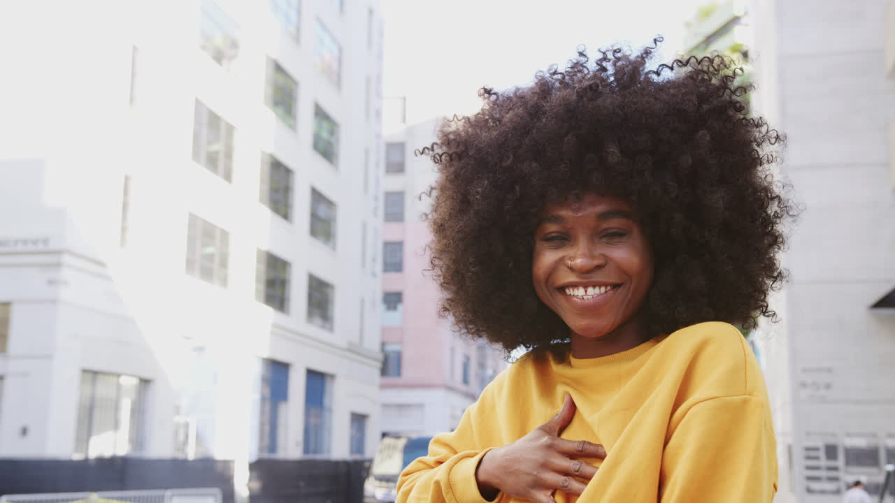 Giovane donna nera con capelli afro e top giallo che ride verso la telecamera per strada