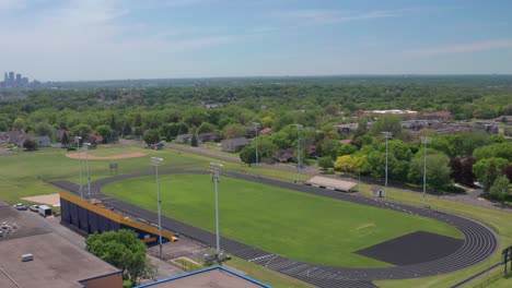 high school bleachers and track in residential neighborhood with city skyline on the horizon- aerial drone flyover shot