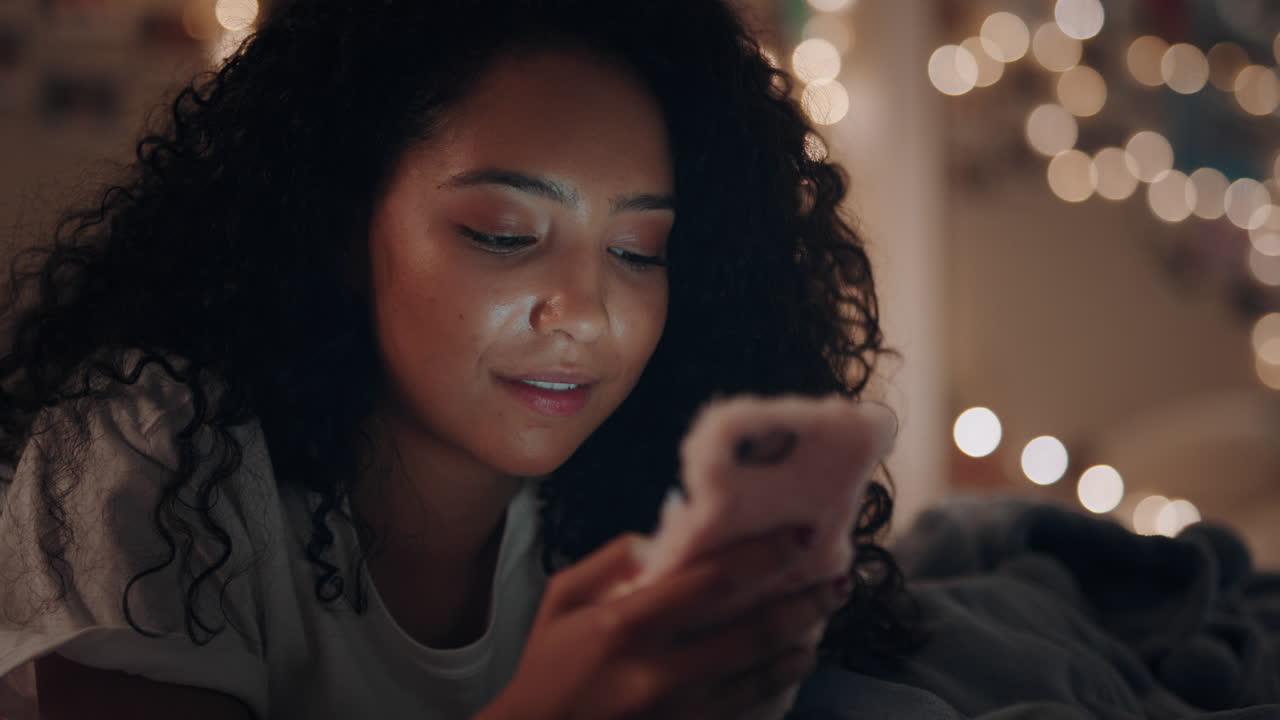 ragazza adolescente felice sdraiata sul letto che invia messaggi usando lo smartphone che naviga sui social media che chatta online che si gode la serata rilassandosi a casa