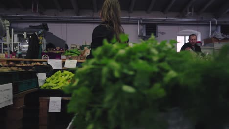 a woman walks among the fruit and vegetable offerings in the covered market