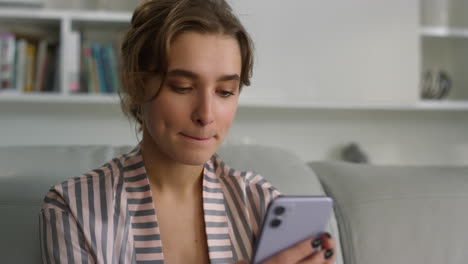 freelancer serio escribiendo mensajes en pijama en primer plano. chica enfocada sosteniendo el teléfono