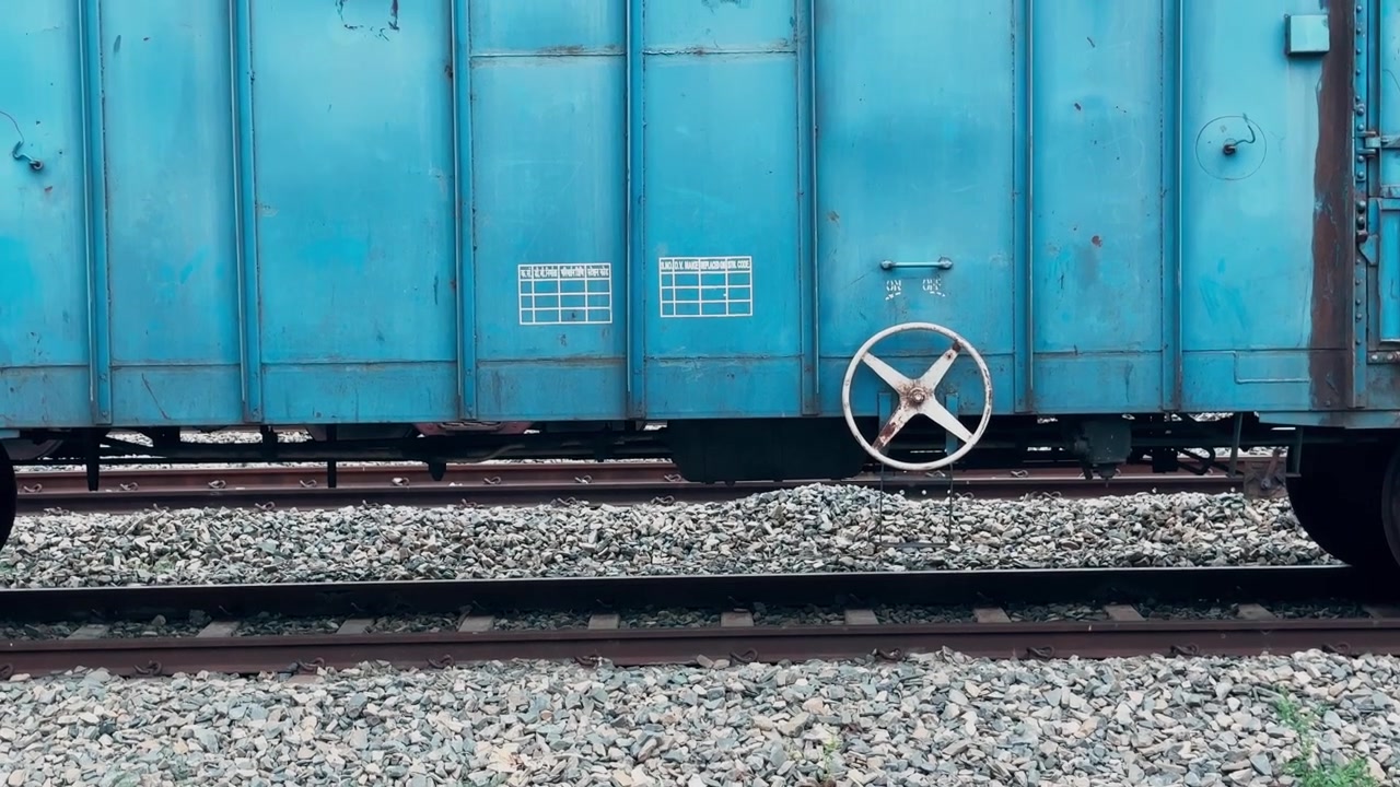 Inquadratura in tilt-up da binari ferroviari multipli a un volantino del freno a mano manuale montato su un vagone merci blu