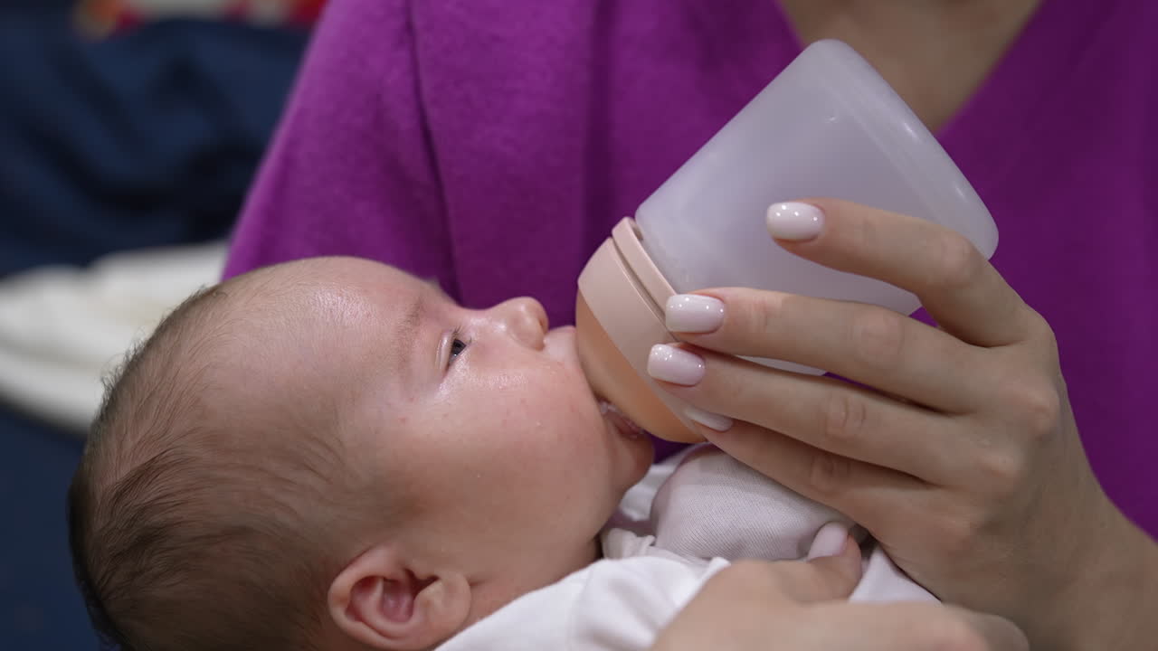 Sweet newborn baby is staying awake while being fed from bottle. Kid suckling milk from a bottle and looking at his mommy. Close up.