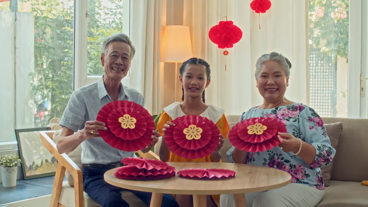 Idosos com a neta mostrando decorações redondas de Tet para a câmera