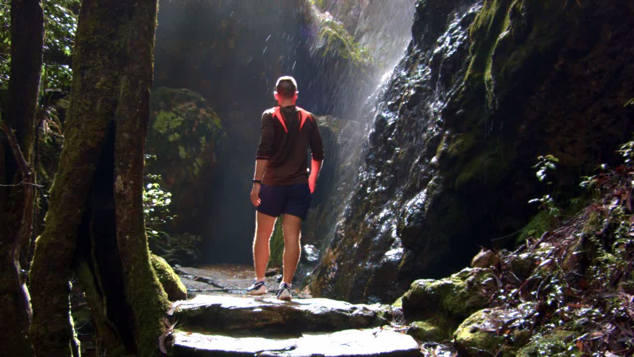 hombre aventurero caminando hacia una cueva rocosa, agua que fluye por las rocas, parque nacional springbrook, australia