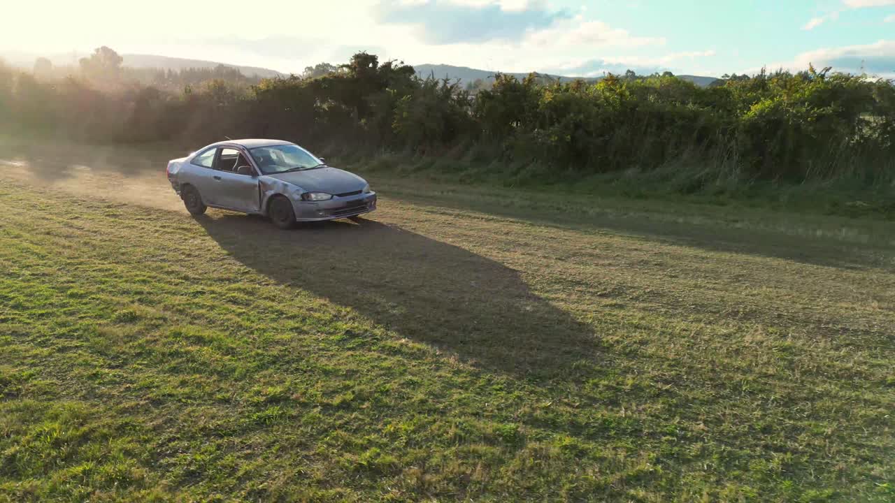 Side angle chase shot of old car racing through field.