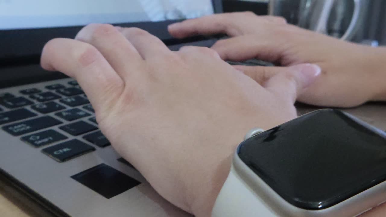 Close-up side view emphasizing the detailed movement of a woman's fingers as she types on a laptop