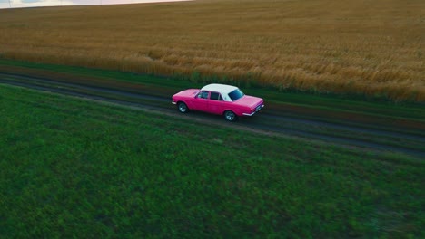 pink vintage car on a country road through a wheat field