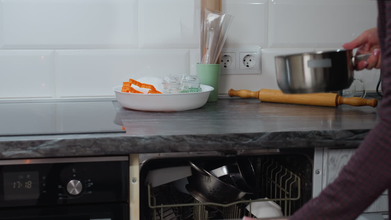 vista parcial individuo quitando la olla de la estufa eléctrica colocándola de nuevo en el armario de cocina abierto con equipos de cocina ordenadamente dispuestos encimera de encimera ardiendo en primer plano