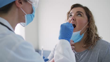 caucasian woman and caucasian female doctor wearing face mask at home using swab test