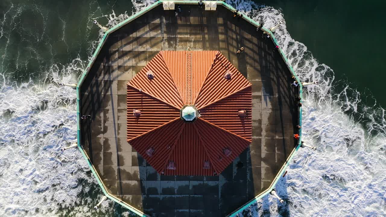 거품이 이는 바다와 파도가 있는 해질녘 맨해튼 해변의 부두 끝에 있는 관광객들과 함께 라운드하운드 수족관의 전망에 접근