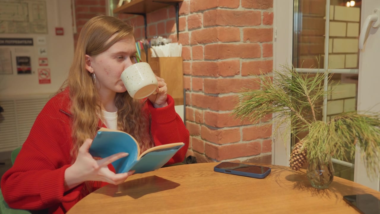 Jovem Mulher Lendo um Livro e Tomando Café em um Café