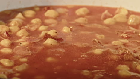 macro close up of brown chicken stock being added to dish with chick peas and bacon