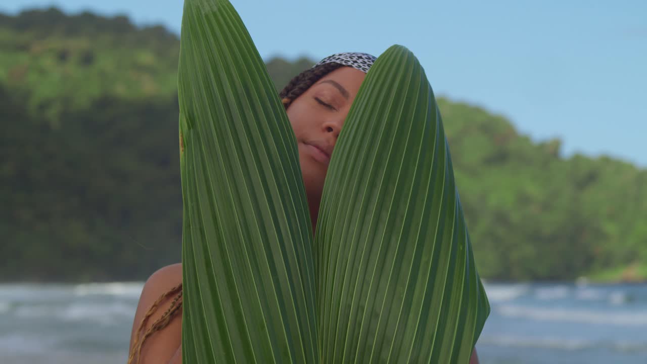 il viso della giovane donna rivela da vicino dietro una foglia di palma sulla spiaggia