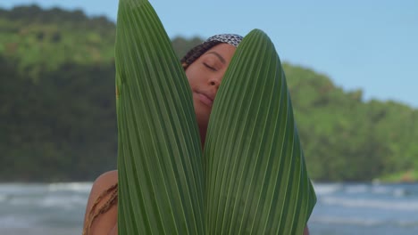 young lady face reveal close up behind a palm leaf on the beach