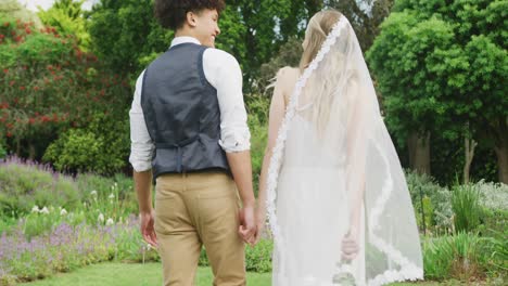 happy diverse couple walking in garden on sunny day at wedding