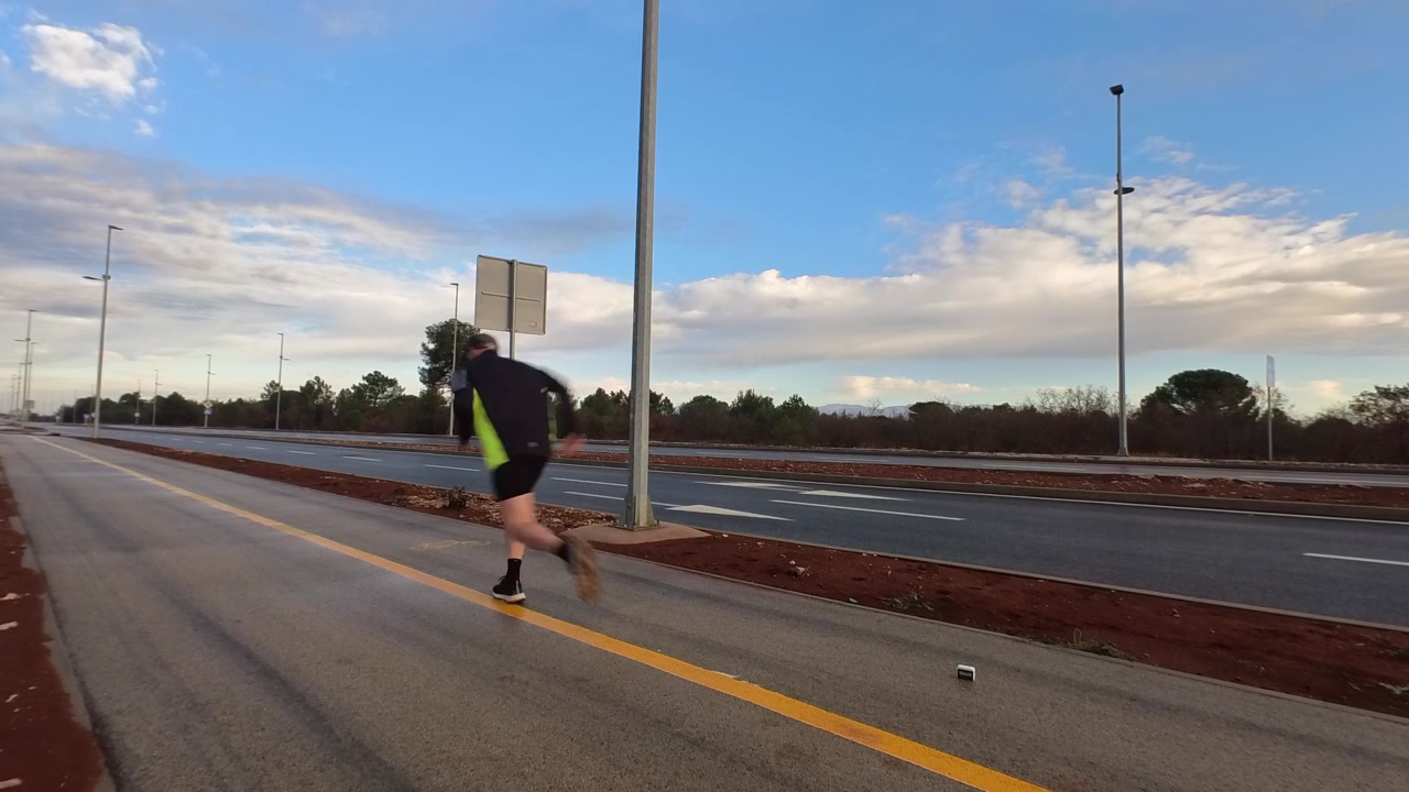 Vista laterale di un corridore che inizia uno sprint da una posizione accovacciata su una strada asfaltata all'alba. Concetto di potenza, allenamento atletico e inizio di una nuova sfida