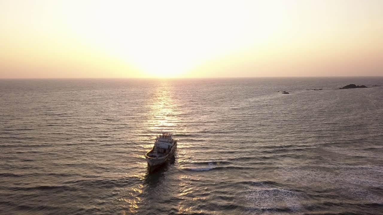 Aerial cinematic circling over wreckage of ship at sunset in Kerala, India