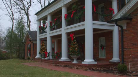 Low-angle-tilt-down-video-of-Fortuna-Missouri-homestead-with-balconies-decorated-with-red-bows-and-two-well-lit-Christmas-trees-in-front-of-the-buildinh-in-rural-Missouri,-USA