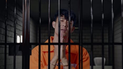 primer plano de un prisionero masculino asiático con esposas de pie en la prisión, haciendo un gesto de la mano de oración pidiendo algo