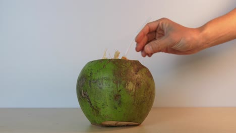 person inserting a straw into a delicious green coconut in slow motion