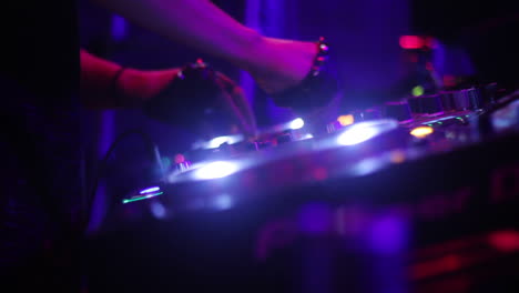 a dj's hands on a mixing console in a dark club setting with purple and blue lights