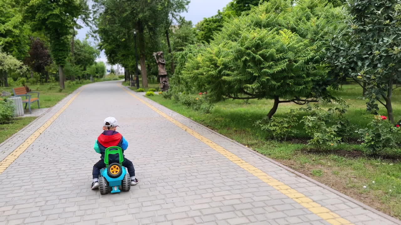 Following a little kid quickly riding on the toy car. Caucasian toddler is on the ride in the park.