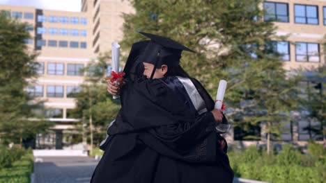 estudiantes asiáticas se gradúan con gorras y vestidos con diplomas sonriendo y abrazándose frente a un magnífico edificio universitario