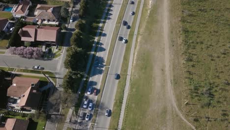 Aerial-Drone-shot-of-highway-with-cars-going-through-and-suburbs-on-side,-tilting-down