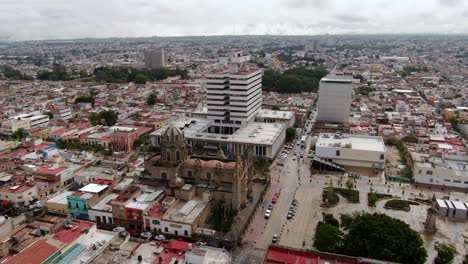 Vista-Aérea-Del-Tráfico-Que-Pasa-Por-El-Santuario-De-Nuestra-Señora-De-Guadalupe,-El-Jardín-Del-Santuario-Y-El-Palacio-Federal-En-Guadalajara,-México