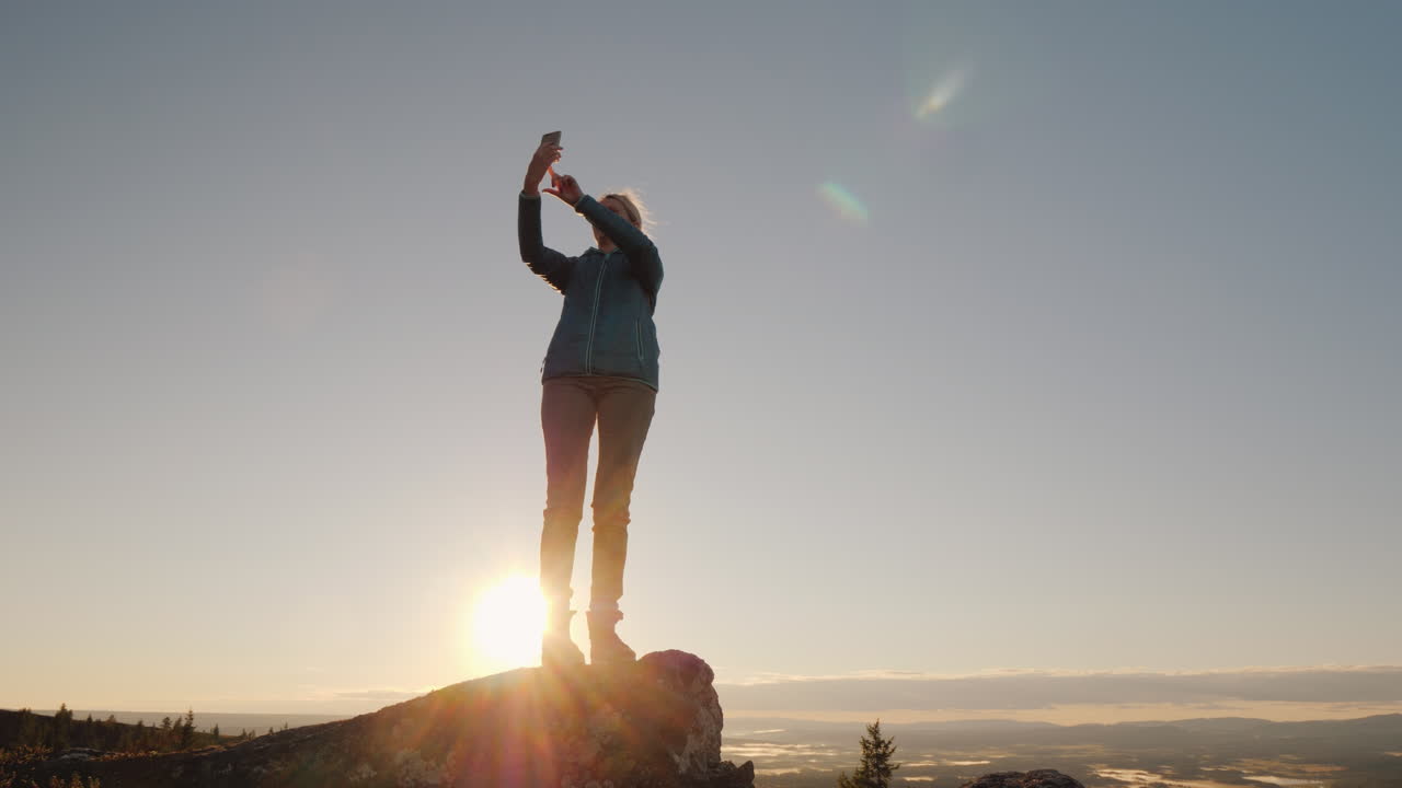 una mujer activa toma fotografías de sí misma en la cima de una alta montaña al amanecer se encuentra en la parte superior de la persona