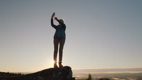 een actieve vrouw maakt foto's van zichzelf op de top van een hoge berg bij zonsopgang staat op de top perso