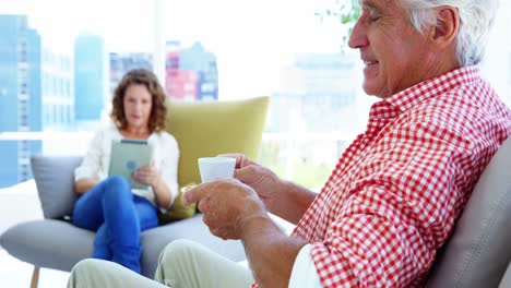 Mature-man-sitting-on-sofa-and-having-a-cup-of-coffee-in-living-room