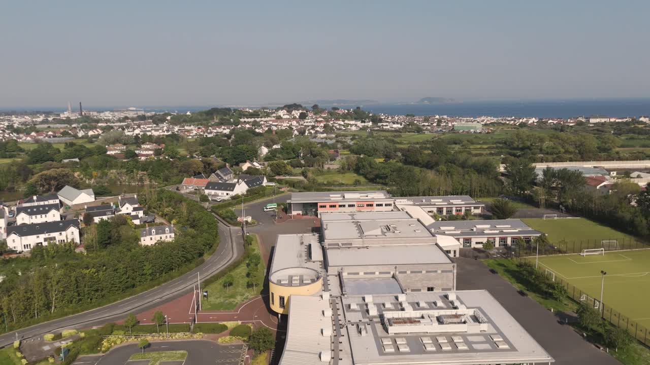 High reveal drone footage of Les Nicolles School,Baubigny,Guernsey showing whole complex and playing fields on bright day