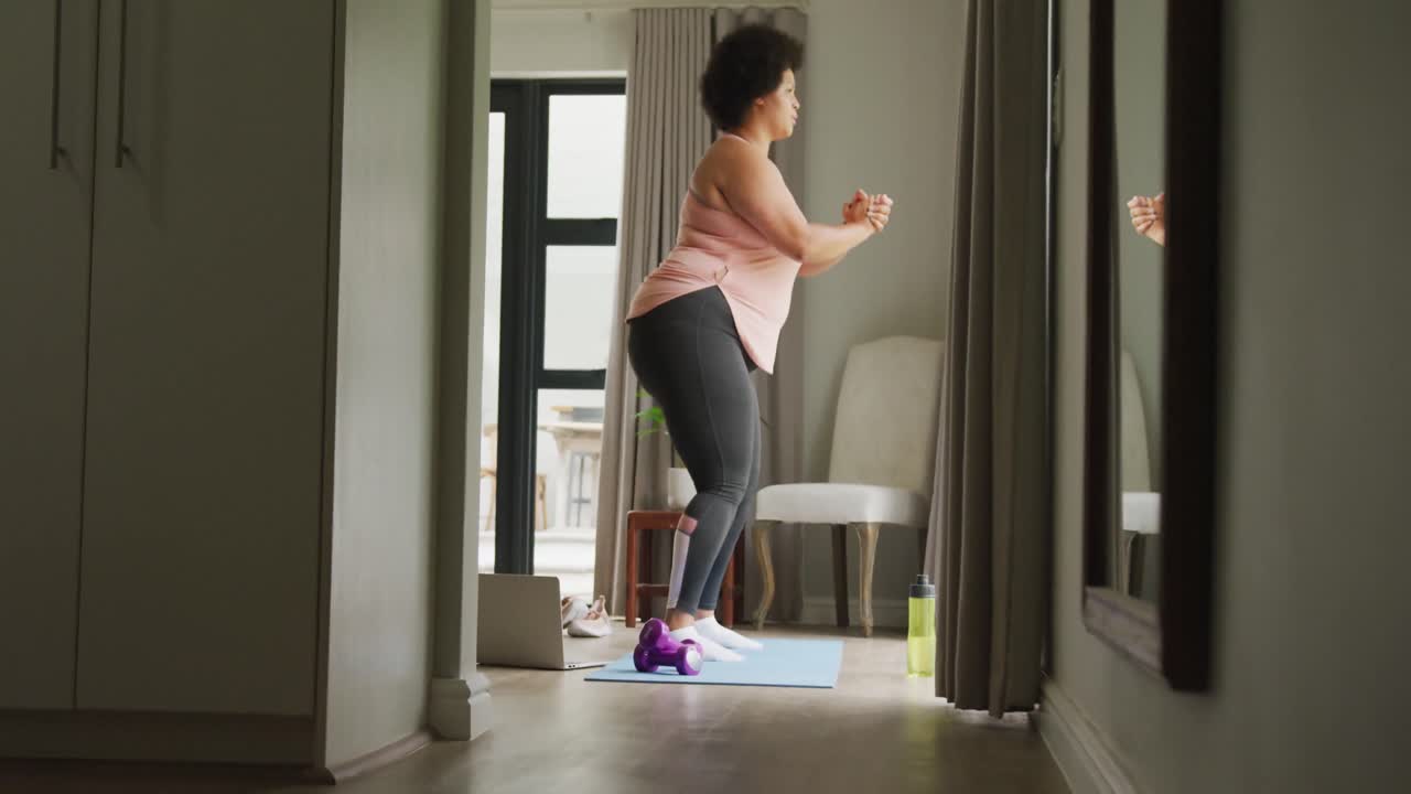 Video di donna afroamericana formosa che si allena a casa, facendo squat.