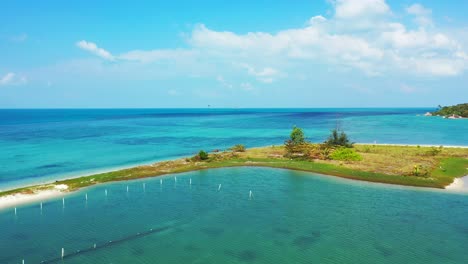 Peaceful-seascape,-calm-clear-water-of-turquoise-lagoon-washing-white-sand-around-tiny-tropical-island,-bright-blue-sky-with-overhanging-clouds,-Thailand