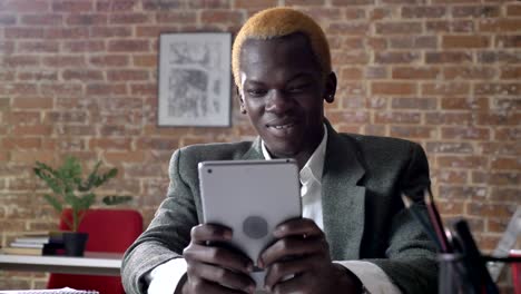 young african american blonde businessman browsing on tablet and smiling, sitting in modern office, confident and successful