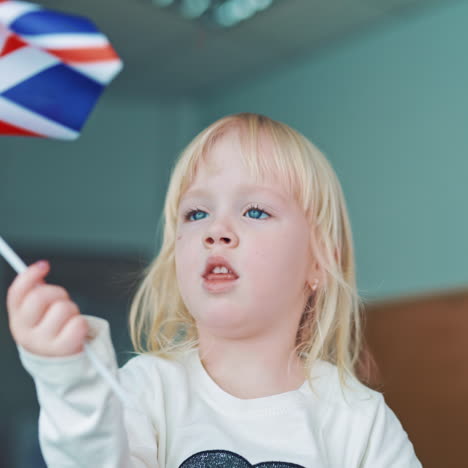 little girl plays with british flag. pretty young child with blond hair holds the flag of great britain. blue,red and white color of the english flag in girl's hands.