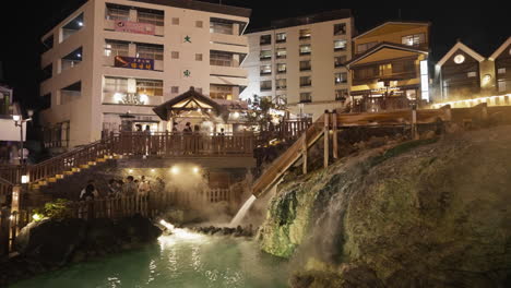 part of kusatsu onsen’s symbolic hot water field at night time with steaming water coming out and tourists taking pictures