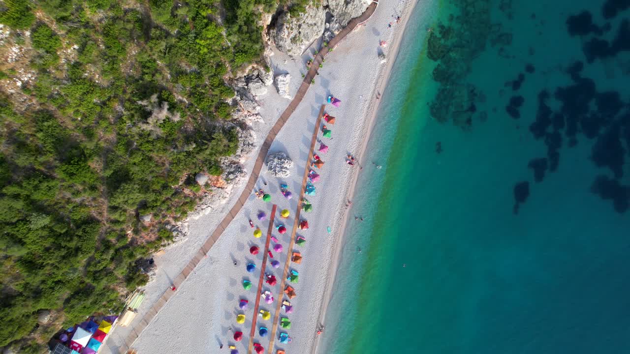 Colorful umbrellas on beach washed by turquoise seawater on rocky shore of Mediterranean in Albania