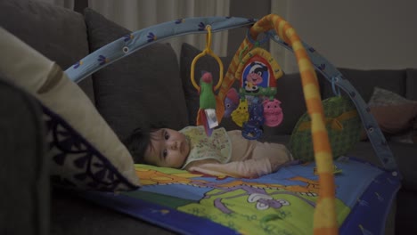 beautiful, cute little baby lying on her play mat with baby activity gym, being happy and looking at the room around her