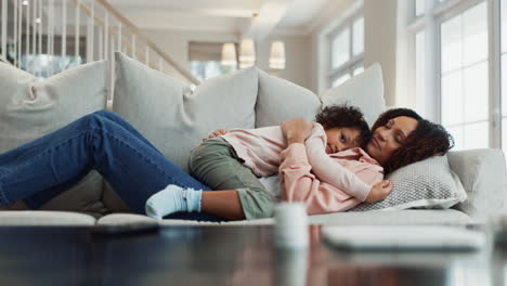 a mother and her young daughter hug and cuddle on the couch at home.